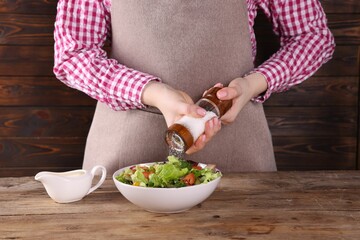 Woman salting tasty salad at wooden table, closeup