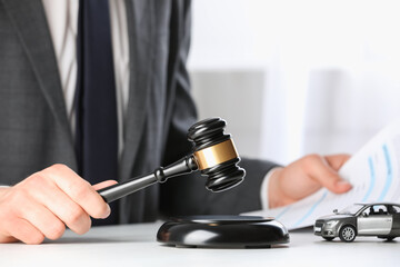 Auto accident law. Man with document striking gavel at table indoors, closeup