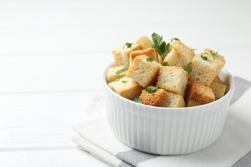 Delicious crispy croutons with parsley on white wooden table, closeup. Space for text