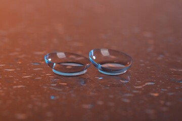 Pair of contact lenses and water drops on color mirror surface, closeup