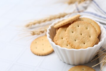 Tasty salty crackers with wheat spikes on white tiled table, closeup. Space for text