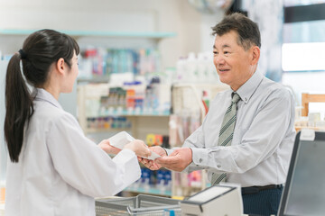 薬局,ドラックストアのレジで処方箋の説明を受けるシニア男性
