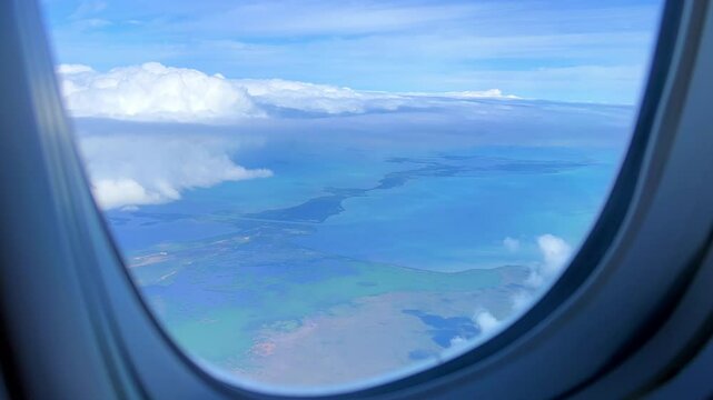 VARADERO, CUBA - DECEMBER 20, 2023: View from the porthole on the Atlantic coast of Cuba. View of the turquoise ocean water and islands with snow-white sand from the plane. White clouds over the water
