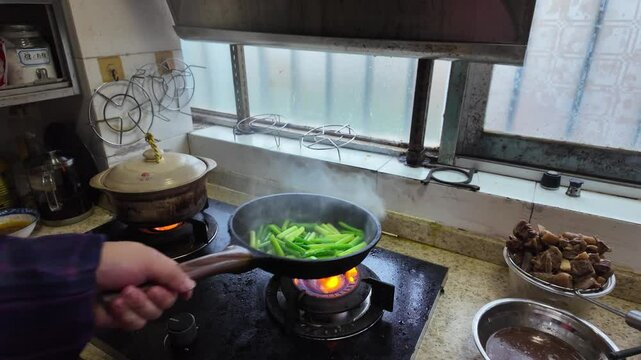 A chef is frying garlic sprouts in a frying pan