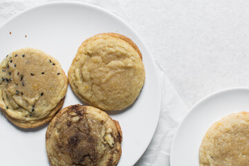 Overhead view of different types of sugar cookies, vanilla cookies, cinnamon cookie, black sesame sugar cookie on parchment paper