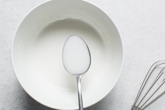 Overhead view of icing sugar mixed with water, powdered sugar dissolved in water on a white table, top view of powdered sugar glaze in a white bowl