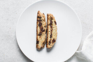 Overhead view of chocolate chip biscotti on white parchment lined tray, top view of chocolate chip cantucci cookies on a white board, flatlay of slices of biscotti cookies or twice baked cookies