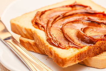 A close-up of a slice of bread with dulce de leche cream on top. Tilted view.