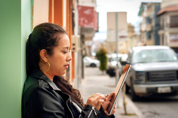 Young latin woman tourist using a tablet while exploring the vibrant city during vacation, surrounded by colorful buildings and parked cars
