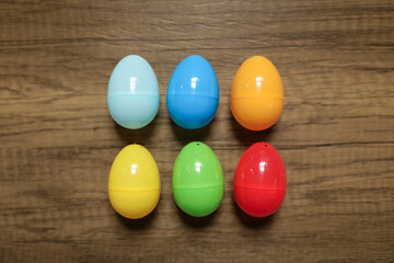 close-up flat lay of plastic red, blue, green yellow and orange Easter eggs in a group against a wooden background 