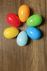 close-up flat lay of plastic red, blue, green yellow and orange Easter eggs in a circle against a wooden background with copy space available 