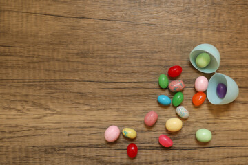 multi-colored jellybeans spilling out of the a light blue plastic Easter egg against a wood background with copy space available