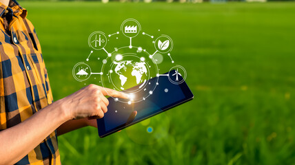 Hand in plaid shirt holding tablet over sunlit grass, glowing eco icons—globe, leaf, turbine—float in harmony, radiating sustainability and digital innovation