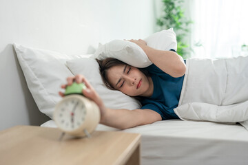 Asian young woman turn off the alarm clock ringing in the morning. 