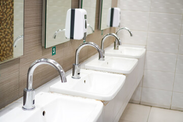 Side view of sinks with faucets arranged in a men's bathroom of public restroom, Thailand.
