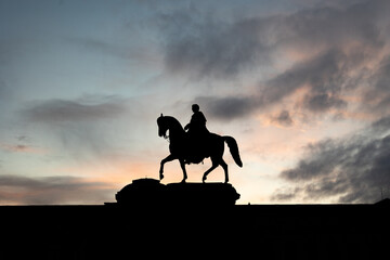 Silhouette of an Equestrian Statue Against a Dramatic Sunset Sky with Moody Clouds