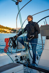 Young man captain standing at the helm and controls a sailboat during a journey by sea in winter time in Montenegro