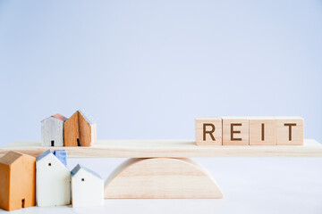Wooden blocks with REIT and houses on balance scale, Real Estate Investment Trust comparison, hedge money during inflation concept

