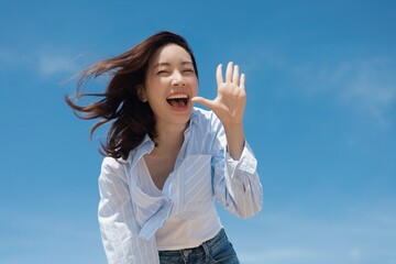 A cheerful Asian woman enjoying a sunny day at the beach. She is wearing a casual shirt and jeans...