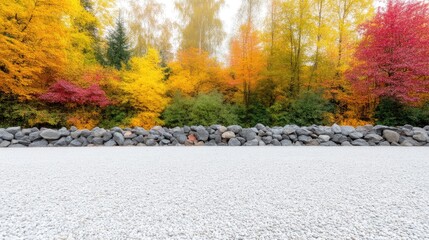 Fototapeta premium Empty white gravel platform bordered by a grey stone wall with a vibrant autumn forest in the background.