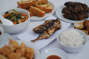 a delicious and diverse Indonesian meal spread. At the center is a plate of two fried mackerel fish, golden and crispy