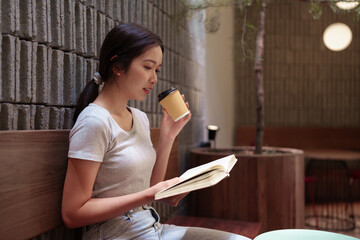 Woman enjoying coffee while reading a book at peaceful outdoor cafe with natural light and wooden...