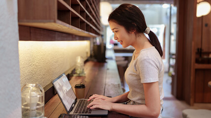 Young woman using laptop and browsing internet at modern cafe counter during casual solo work session