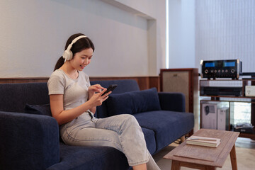 Obraz premium Young woman relaxing on sofa while listening to music with headphones and browsing songs on smartphone.