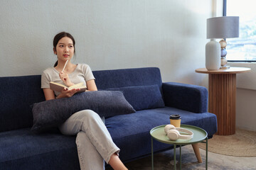 Obraz premium Calm young woman sitting on couch and writing in her diary during a peaceful moment in cozy home setting