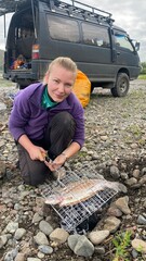 A girl fries fish on a fire