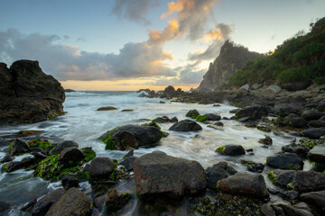 The orange light of the sunset on the horizon of Watu Lumbung Beach, combined with the sound of waves crashing against the sturdy coral cliffs.