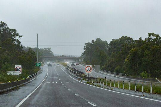 Rainy stormy day with cars driving on wet highway road with 80 speed zone signs