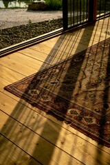 Golden light of sunset streaming through vertical bars onto a vintage Persian rug on a wooden floor