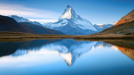 Beautiful mountain peak with its reflection in a lake at sunrise. The focal point is on the snow-covered peaks during the autumn season