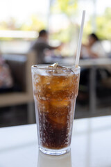 A glass of ice-cold cola sits on a table, condensation glistening on the glass.