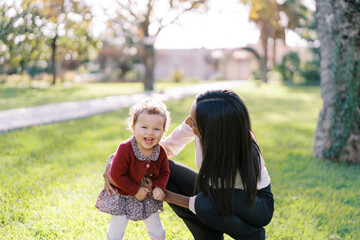Mom tickles a little laughing girl sitting next to her on the grass