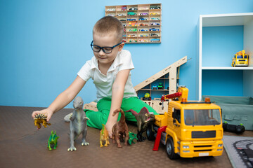 Boy with glasses plays with dinosaurs and cars in his room, selective attention to toys, bright colors, the concept of childhood and games.
