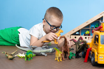Boy with glasses plays with dinosaurs and cars in his room, selective attention to toys, bright colors, the concept of childhood and games.