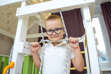 Boy performs gymnastic exercises on a wooden home sports complex with stairs and a slide. Sports exercises for children. Physical education of children at home