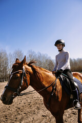 The training process. A young teenage girl jockey in a helmet rides a horse on a sandy arena, training at a riding school. The concept of horse riding training. Jumping competition.