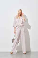 Stylish woman posing against a white wall in a wide beige blouse and trousers
