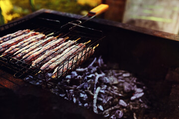 Selective focus. Cooking barbecue on the mangal in nature. Grilled tasty meet cooking on the party. Traditional Russian shashlik on a barbecue skewer on sunny forest.