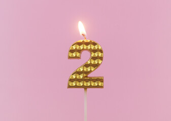 Burning gold birthday candle on pink background, number 2