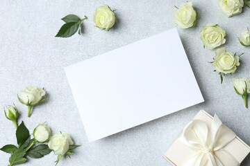 Beautiful white roses with paper card and gift box on gray background