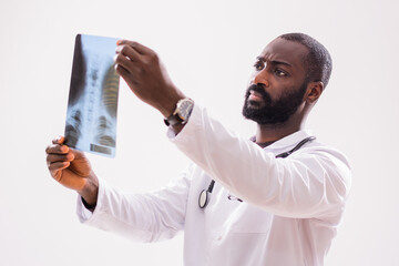 Portrait of serious African radiologist who is holding and looking at x-ray image on gray...