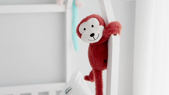 Smiling red monkey plush toy clinging to a white crib rail in a softly lit nursery