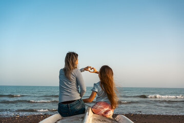 Mother and daughter making heart shape on the beach.