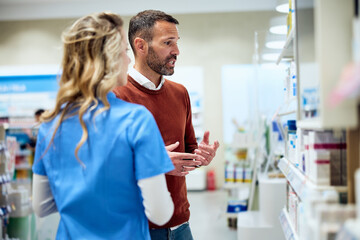 Fototapeta premium Pharmacist Assisting Pharmacy Customer While Explaining Medication Options Inside Modern Pharmacy