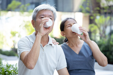 Old man and woman, Asian senior couple drinking water from paper cup together, outdoor scene