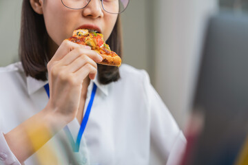 Asian businesswoman eating pizza while working with clients due to rush hour.